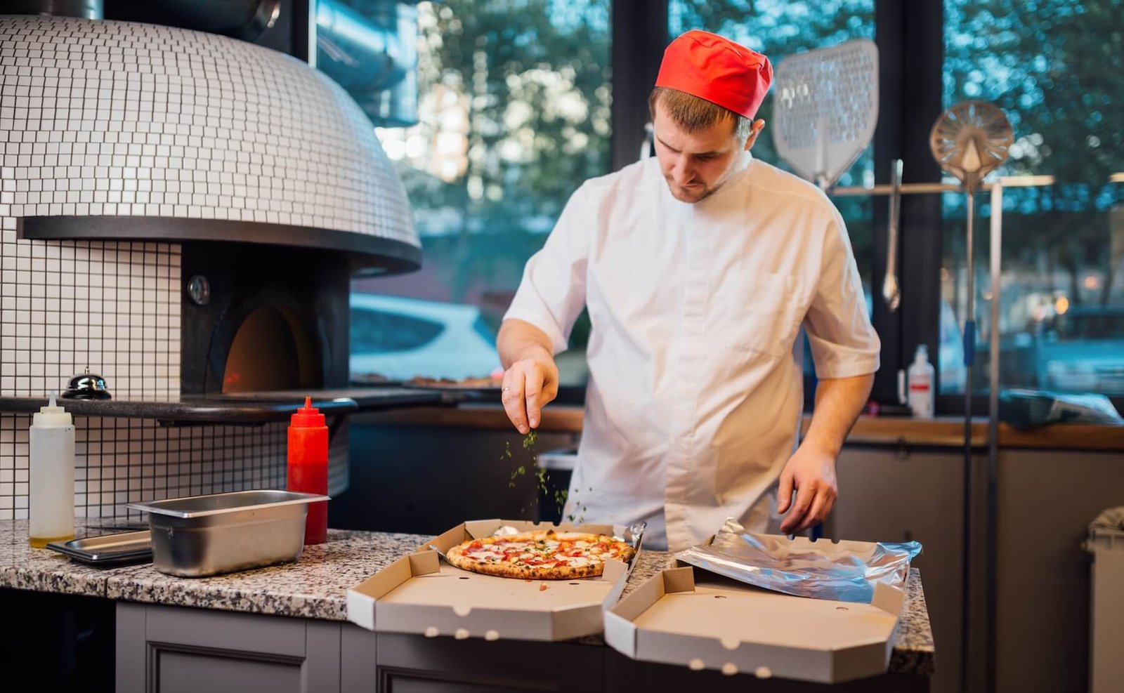 Chef finishing a pizza beside a tiled oven